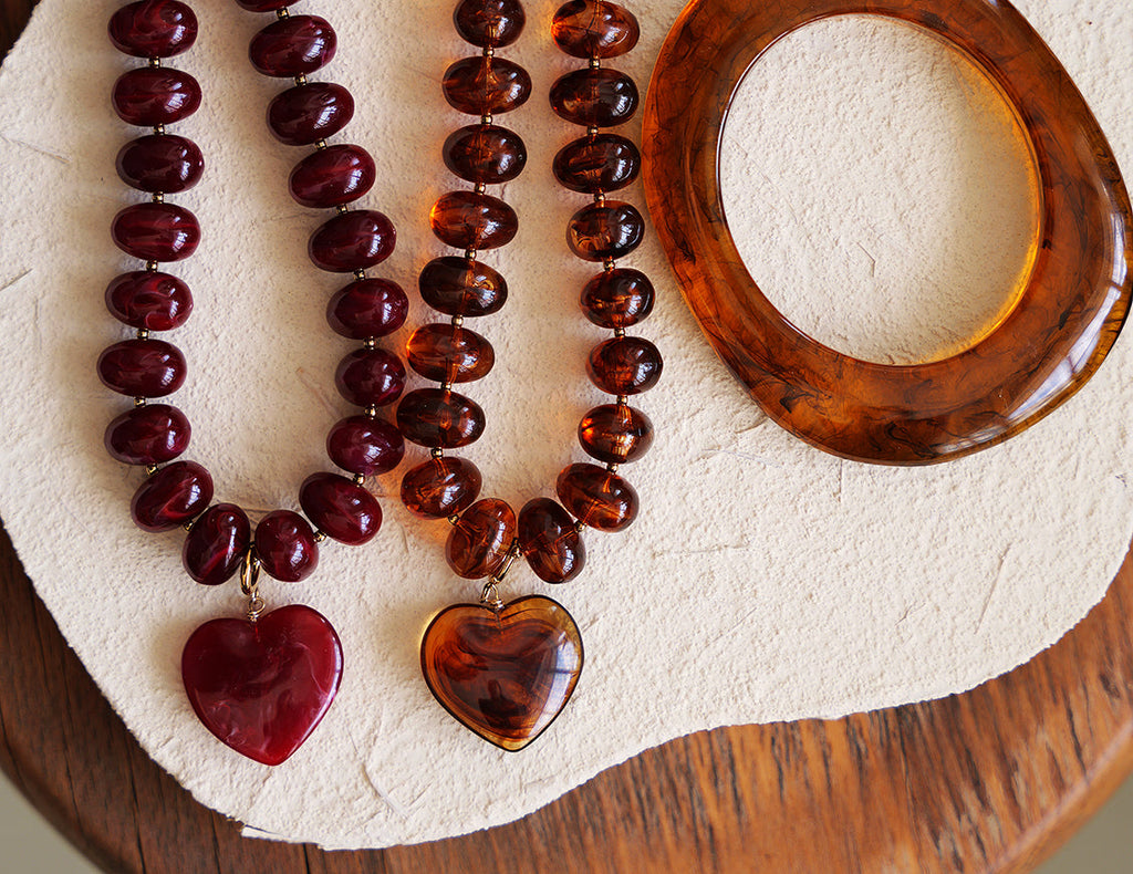 Two necklaces with heart pendants and a tortoiseshell bracelet on a textured surface.